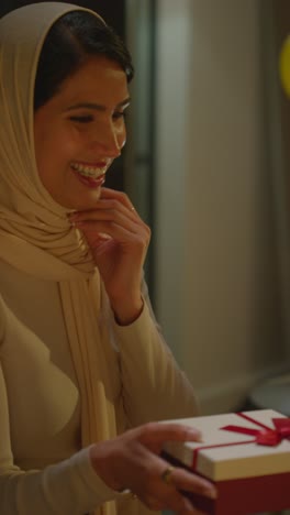 Vertical-Video-Of-Woman-Wearing-Hijab-Receiving-Birthday-Present-At-Home-With-Party-Balloons-In-Background