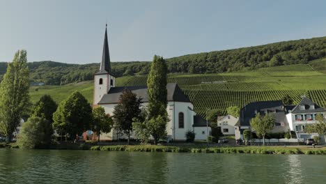 scenic view of a church at a river bank with vineyards in the background