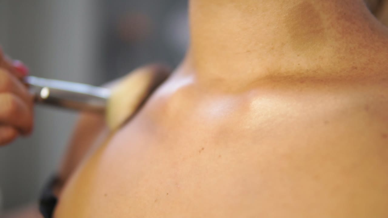 Close Up view of a brush applying golden powder on the model's neck and chest. Professional make up. Slow Motion shot