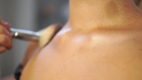 Close-Up-view-of-a-brush-applying-golden-powder-on-the-model's-neck-and-chest.-Professional-make-up.-Slow-Motion-shot
