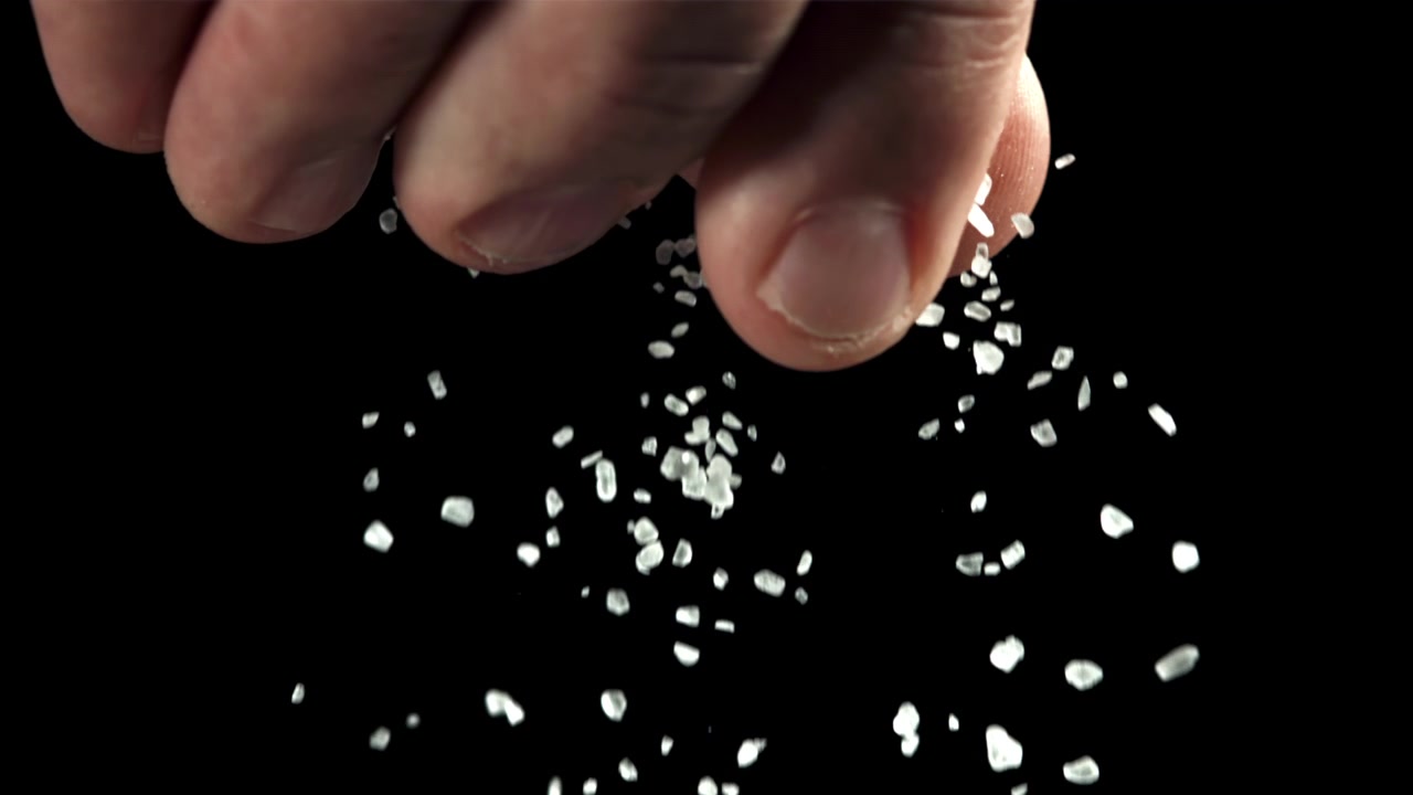 Gros plan d'une main saupoudrant de gros sel blanc sur fond noir