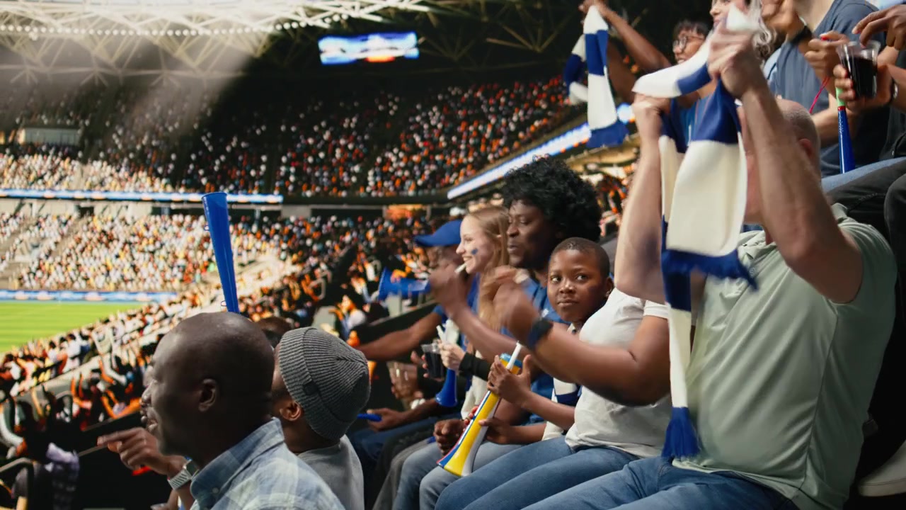 Joven aficionado al fútbol animando con aficionados azules durante un partido de fútbol en vivo.