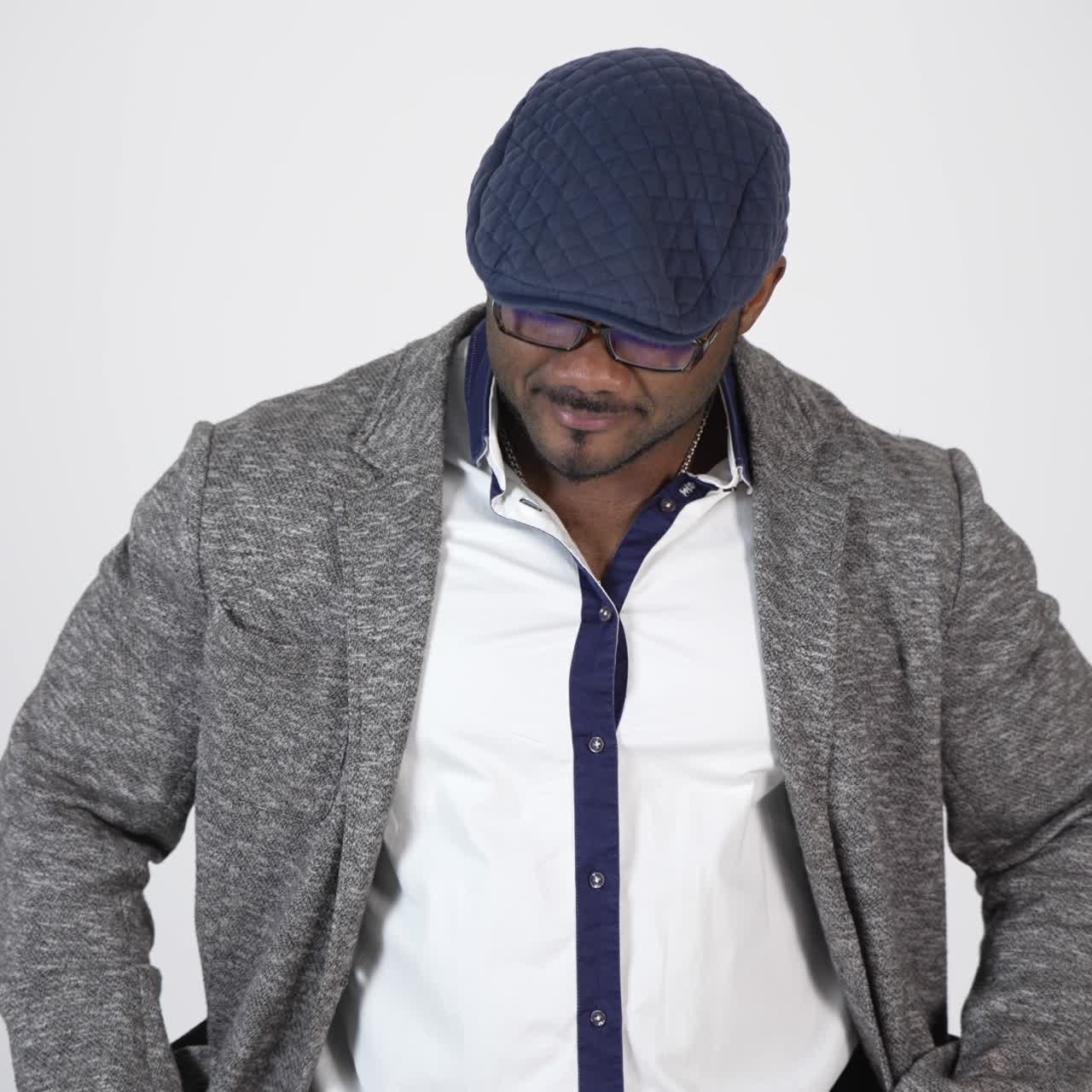 Elegante uomo afroamericano si mette il cappellino su sfondo studio. Uomo d'affari afroamericano con cappellino e occhiali è in piedi da solo e guarda in camera. Slow motion.