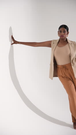 vertical video: confident woman posing in stylish outfit, leaning gracefully in studio