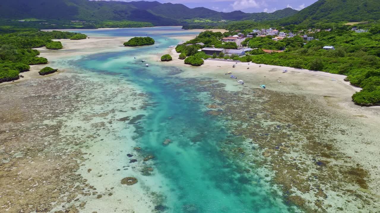 breathtaking aerial drone shot slowly flies over the world-renowned Kabira Bay on Ishigaki Island, Japan. The footage captures the striking contrast between the deep, turquoise blue channel
