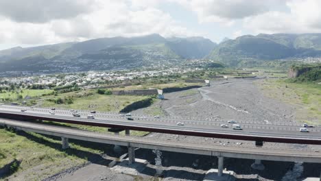 Drone-shot-of-a-highway-bridge-on-Reunion-Island,-France-with-beautiful-landscape-of-mountains-at-background