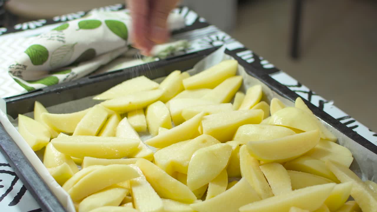 Putting salt on cut potatoes in a tray, to cook them in the oven.