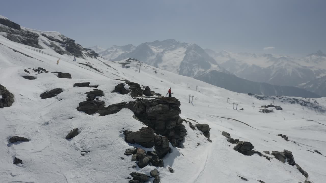 Person Standing on a Cliff Overlooking a Snow-Covered Mountain Range