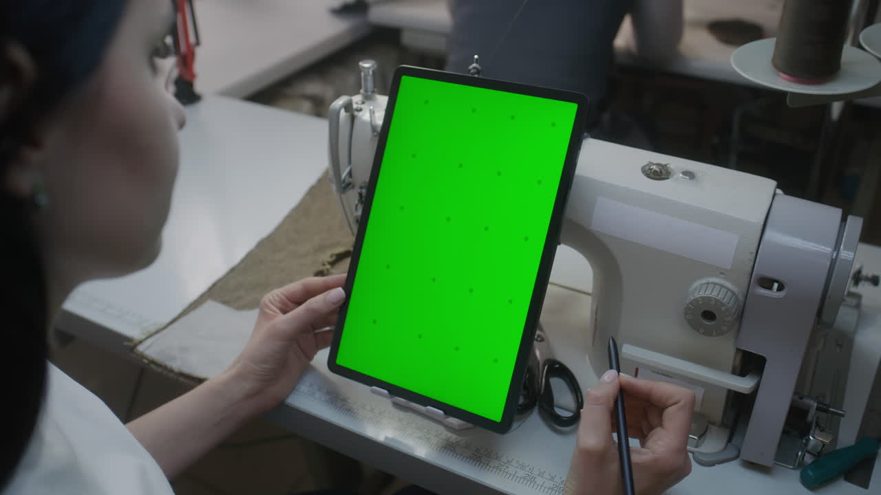Woman using tablet with green screen at a sewing machine