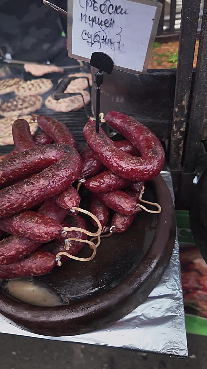 Panoramica verticale su carni alla griglia su una bancarella durante un festival culturale bulgaro. Utile per servizi di viaggio, reportage culinari e copertura documentaristica della cucina locale.