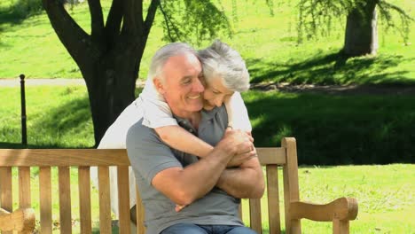 Woman-hugging-her-husband-sitting-on-a-bench