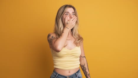 smiling young woman standing with widened eyes on yellow background