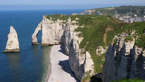 Panning-drone-shot-of-stunning-sea-cliff-formation-and-Etretat-City-in-background-during-sunny-day,-France