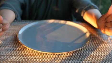 person holding a fork at an empty plate ready to eat