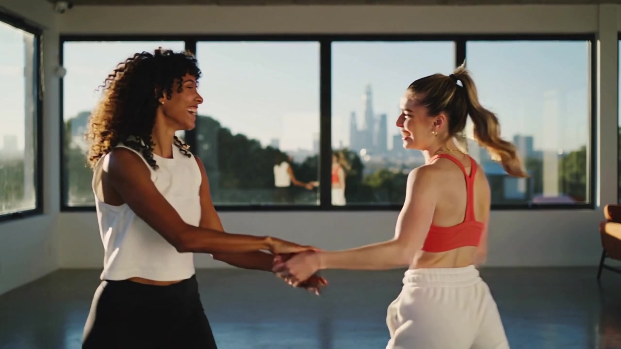 Lifting left arm, right woman practicing dance in studio, turning partner by windows in sportswear