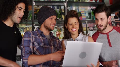 amigos interactuando entre sí mientras usan una computadora portátil en un pub
