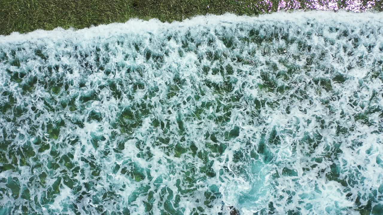 Seascape texture with waves foaming over coral reefs and pebbles seen through clear turquoise water on coastline of Bahamas