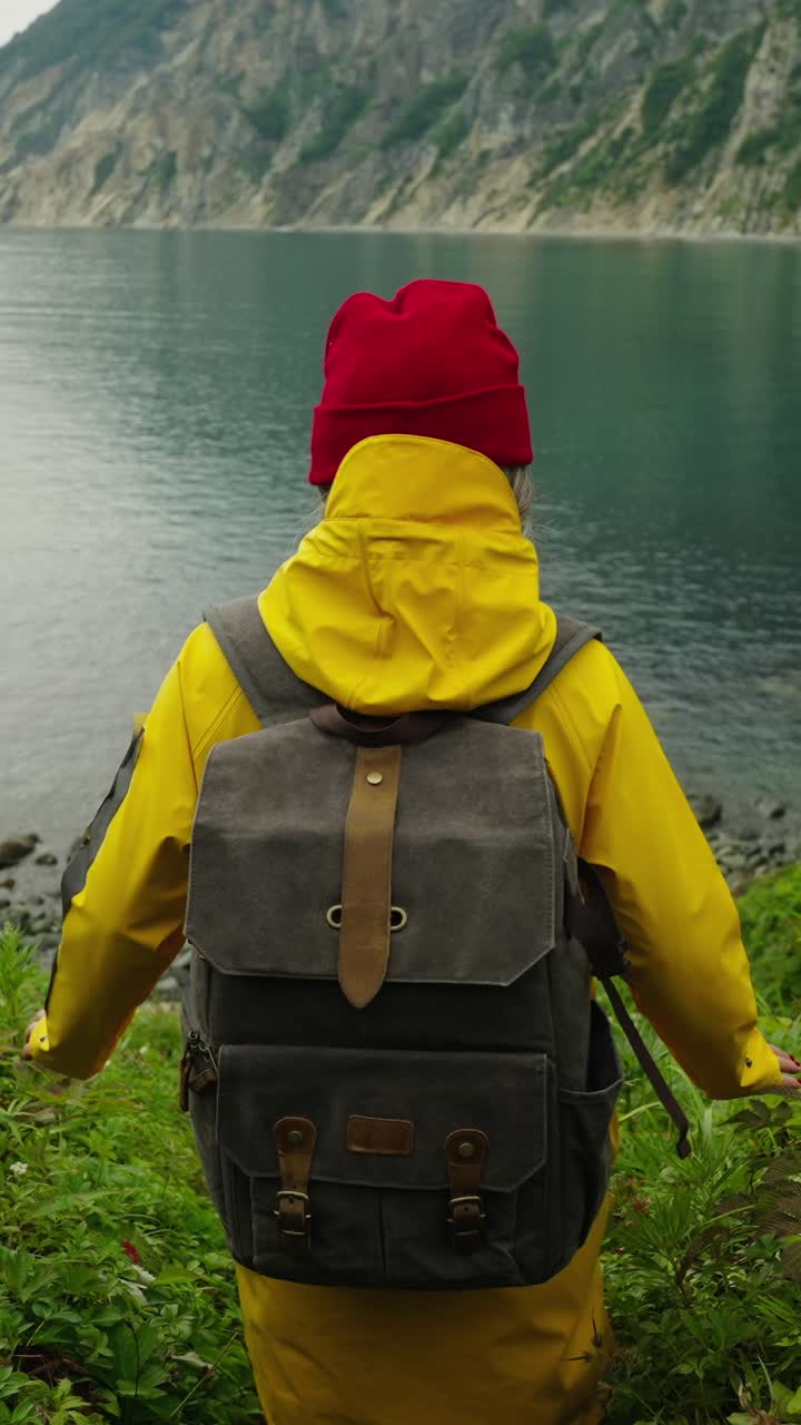 Escursionista con impermeabile giallo e zaino che guarda il panorama di un lago di montagna