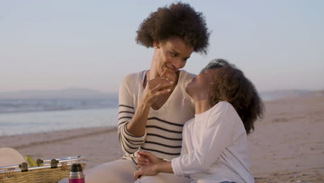 loving mother and daughter sharing a croissant and having fun during a picnic on the beach