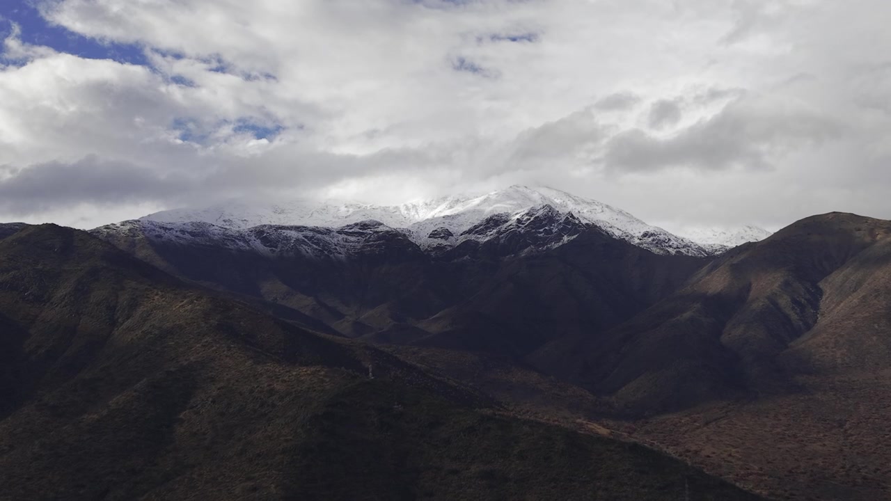 Tomada de drone em alta altitude voando em direção ao terreno acidentado e picos imaculados cobertos de neve da Cordilheira dos Andes perto de Santiago