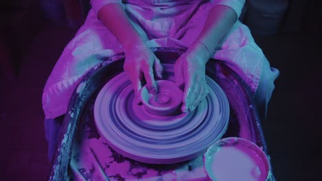 young woman potter working with a wet clay in neon lighting