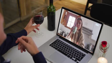 Mixed-race-man-sitting-at-table-using-laptop-making-video-call-with-female-friend