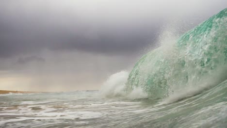 Large-rough-shorebreak-wave-crashes-down-on-cloud-filled-stormy-sky