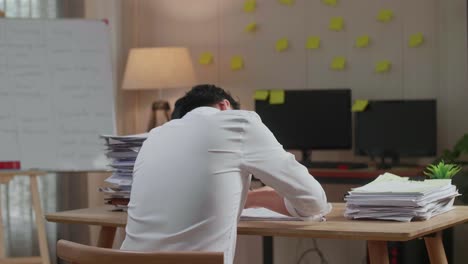 back view of asian man yawning before sleeping while working hard with documents at the office