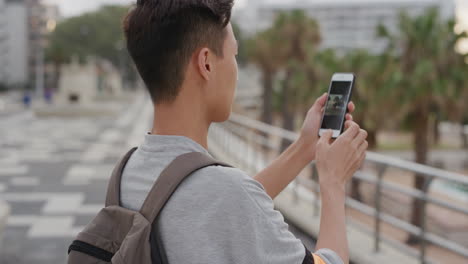 portrait young asian man tourist using smartphone taking photo of vacation experience enjoying sharing photography smiling cheerful urban city seaside