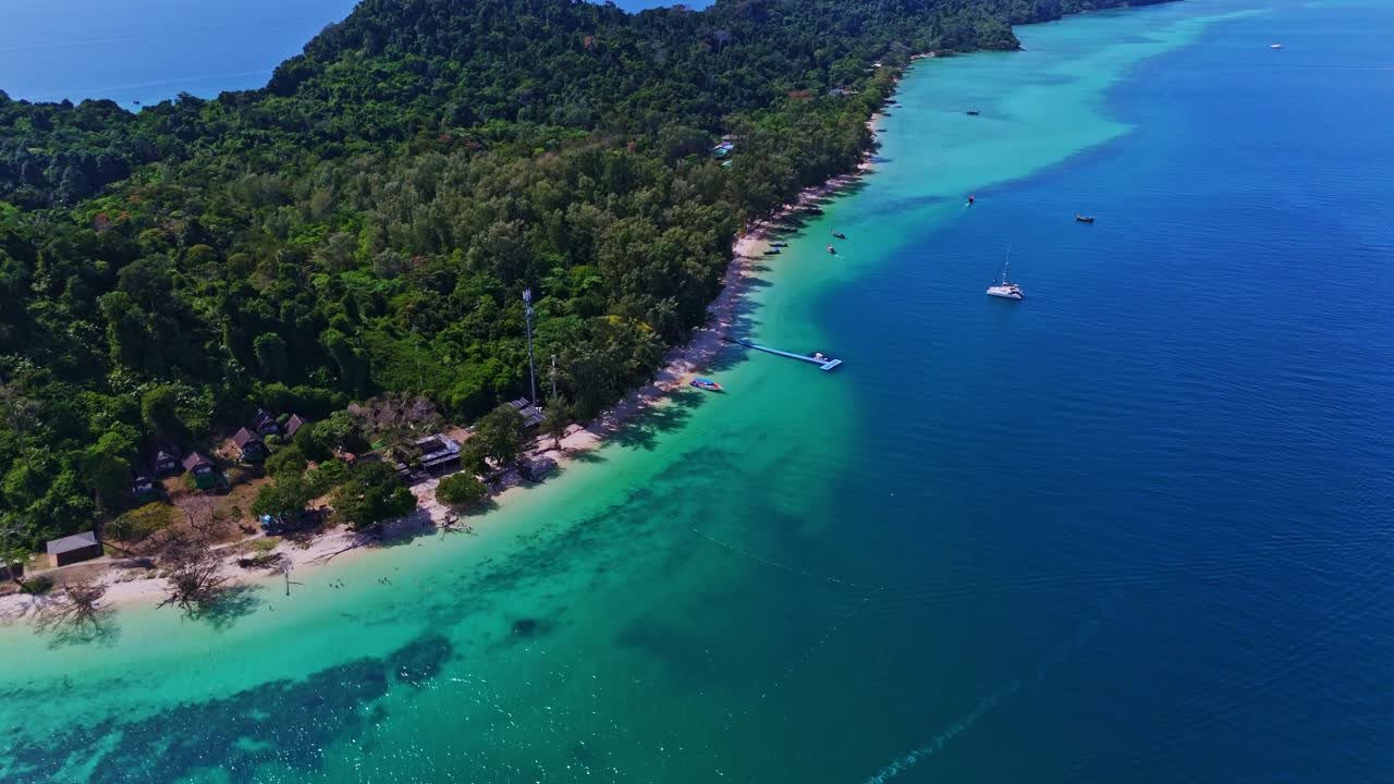 Aerial drone shot of Koh Kradan, Thailand, highlighting beachfront bungalows, turquoise waters, a floating pier, and lush tropical greenery in a serene island paradise in 4K.