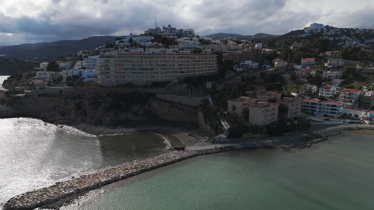 Wide establishing of Playa Sur shoreline and cityscape under cloudy skies in Peniscola, Spain