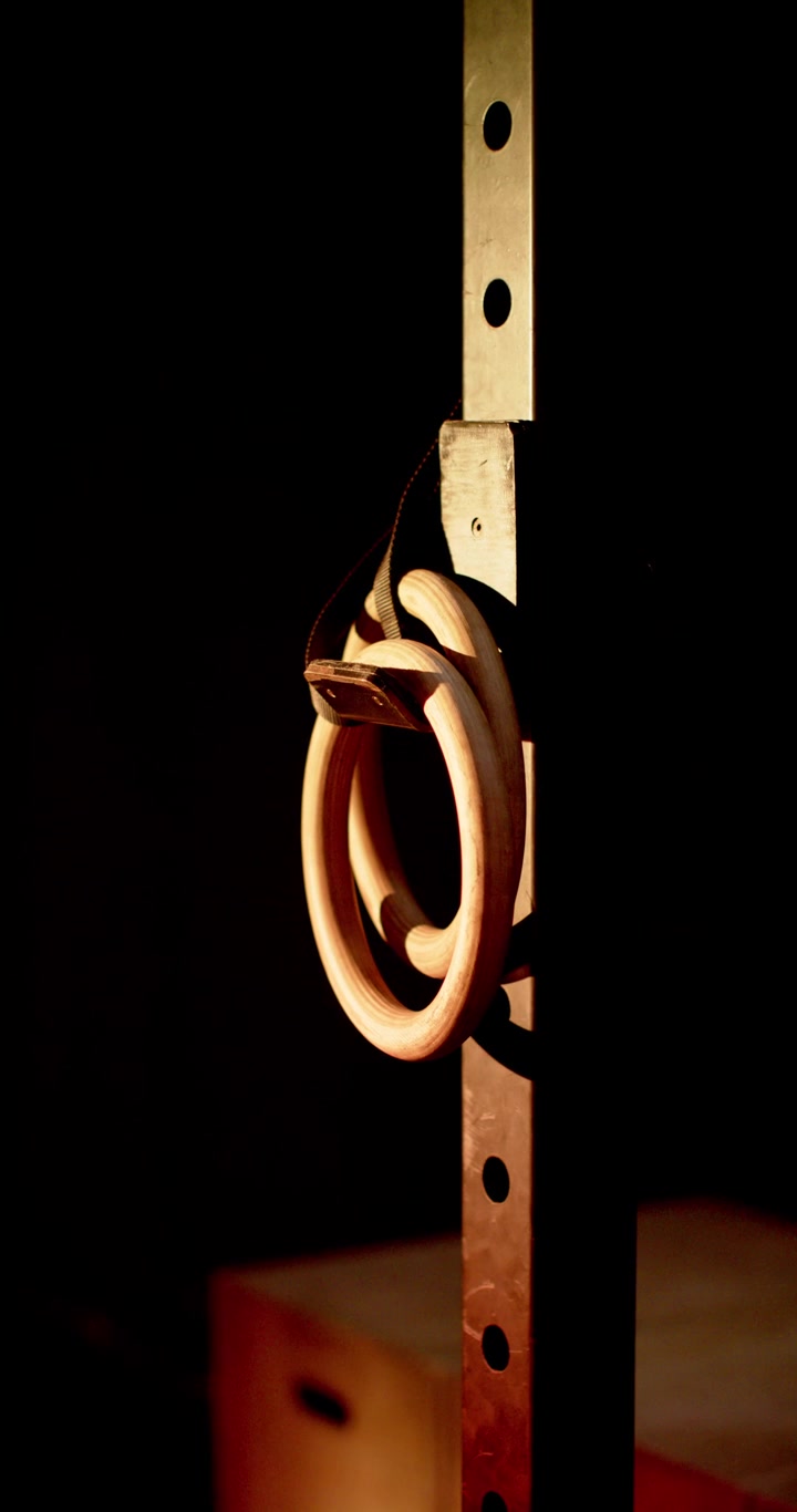 Vertical video: Rings are swaying from subtle shifts on metal rack as warm light is casting shadow