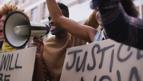 hombre afroamericano gritando usando megáfono con otras personas levantando los puños durante la protesta