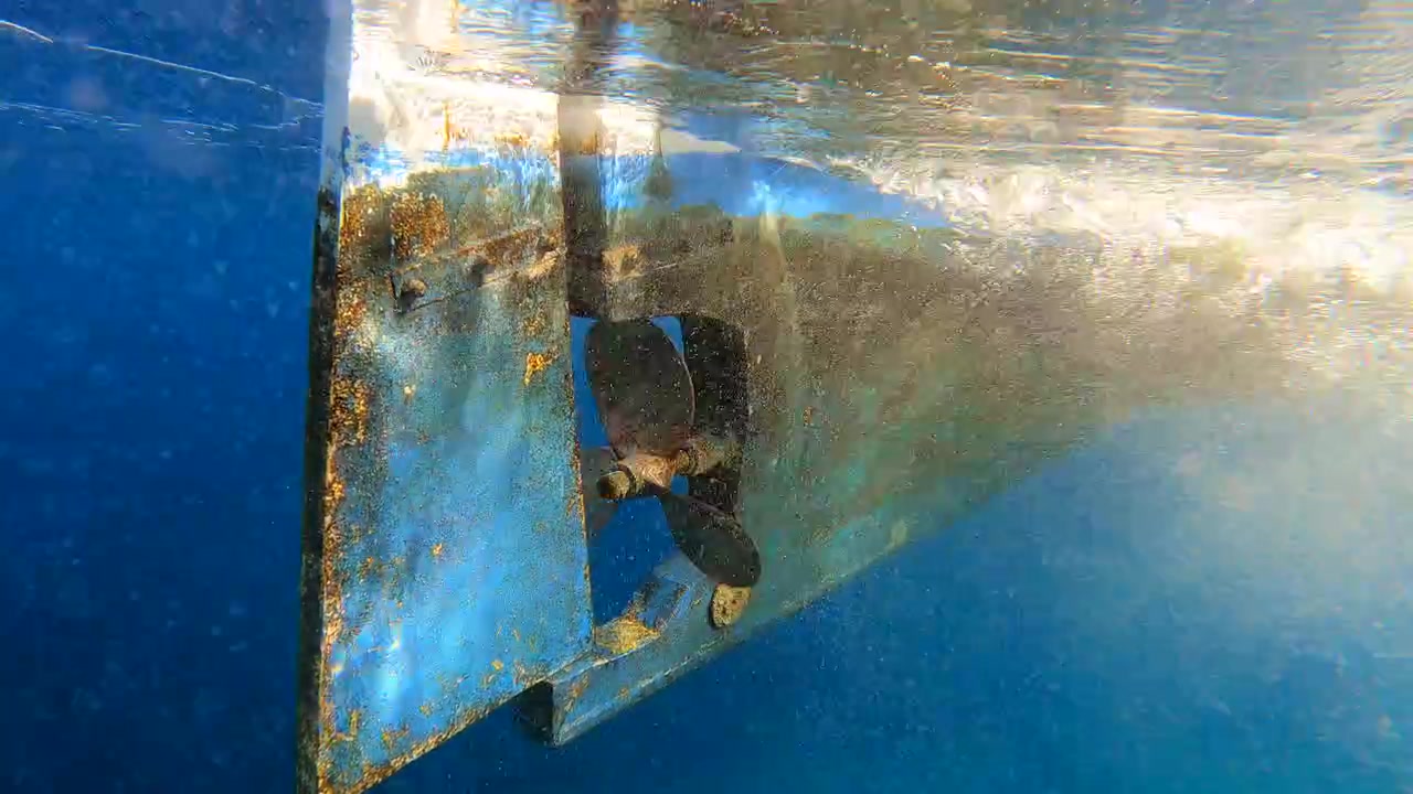 透明な青い水中で回転する船のプロペラ（水中視点）