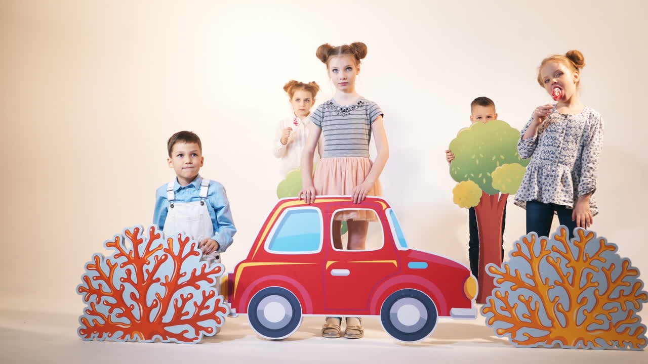 Friends are playing in the childish studio. Two girls eating tasty lollipops. Beautiful toyful decorations and children on the white studio background