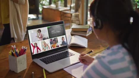 Schoolgirl-using-laptop-for-online-lesson-at-home,-with-diverse-teacher-and-class-on-screen