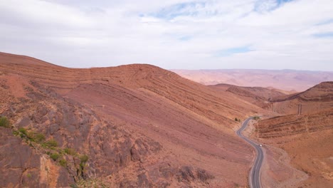 Descending-aerial-view-of-asphalt-road-surrounded-by-massive-Atlas-Mountain-Scenery-during-sunny-day-in-Morocco,Africa