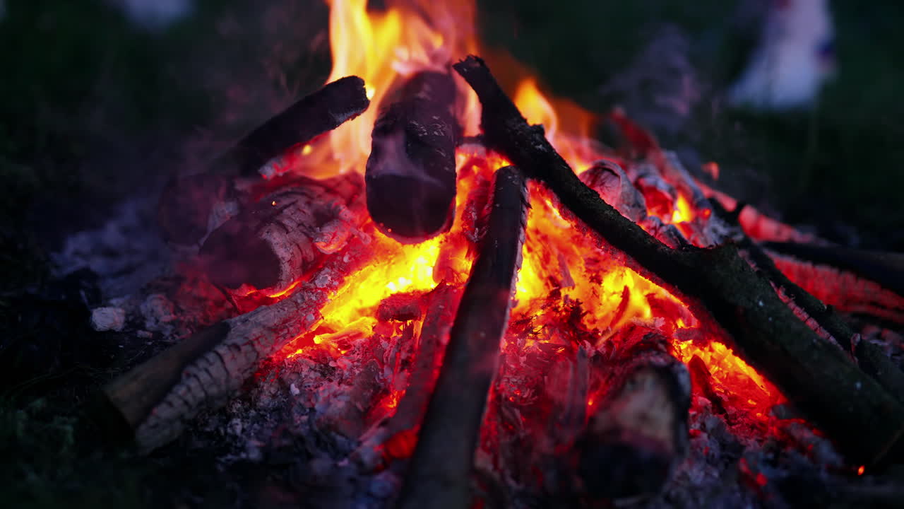 Beautiful bonfire on dark background. Red and yellow flame with smoldering logs at night. Romantic campfire in summer evening. Close-up.