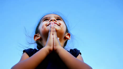 child praying with joyful expression under clear blue sky