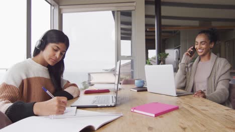 Video-of-focused-biracial-women-working-from-home-with-laptop-and-smartphone