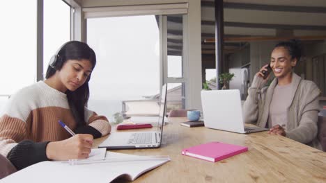 video de mujeres biraciales enfocadas trabajando desde casa con portátiles y teléfonos inteligentes