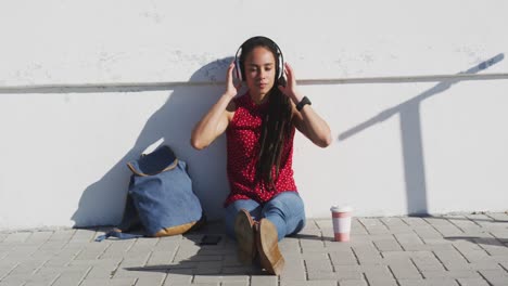 African-american-woman-wearing-headphones-and-listening-to-music-on-promenade-by-the-sea