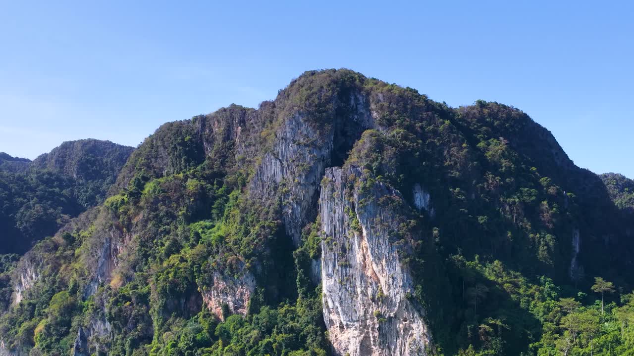 Sebuah aerial drone shot lambat bergerak menuju tebing batu kapur hijau subur di bawah langit biru cerah