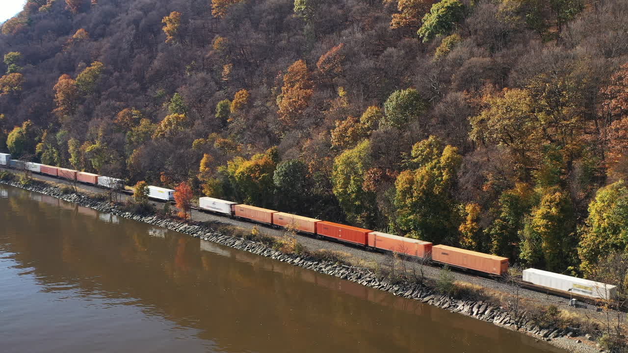 An aerial view from the south side of the Mid-Hudson Bridge. The camera pans left looking towards Highland Landing on the west bank of the Hudson River. There is a long cargo train - It's a sunny day.