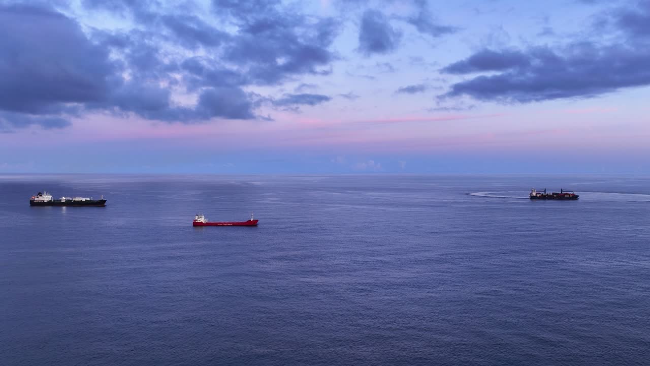 Top aerial view at blue hour of three cargo ships anchored in open ocean