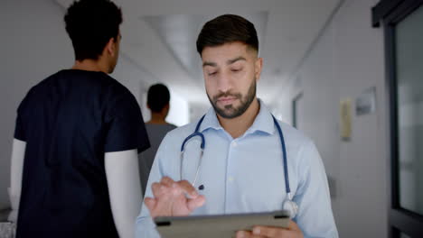 Un-Joven-Médico-Asiático-Con-Traje-Médico-Revisa-Los-Datos-Del-Paciente-En-Una-Tableta.