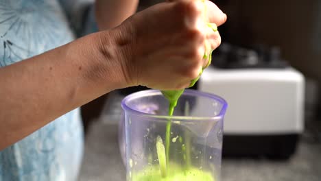 manos exprimiendo jugo verde en tela de queso