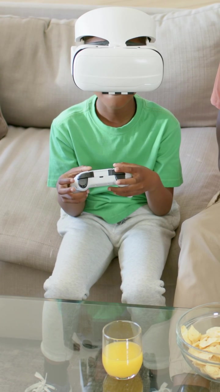 Vertical video: Holding controller kid in green tee with VR set adjusting grip at home with adult