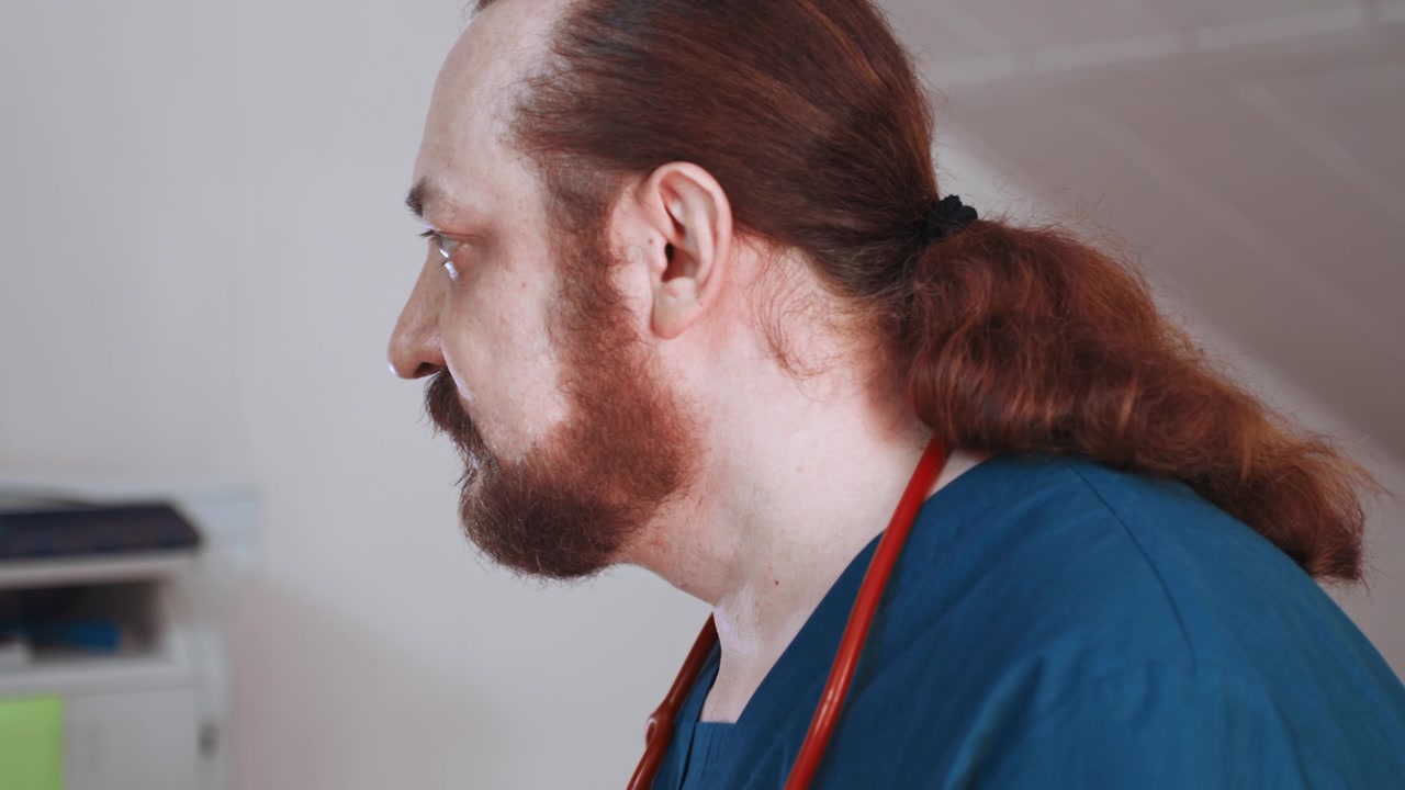 Paramedic home assessment profile close side view showing bearded clinician with ponytail and stethoscope, reviewing notes in residential interior, calm focused expression, supportive caregiver