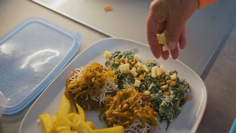 agregando queso a las espinacas con nueces de pino, en un plato donde también hay hamburguesas con cebolla, pimientos y queso, y papas fritas